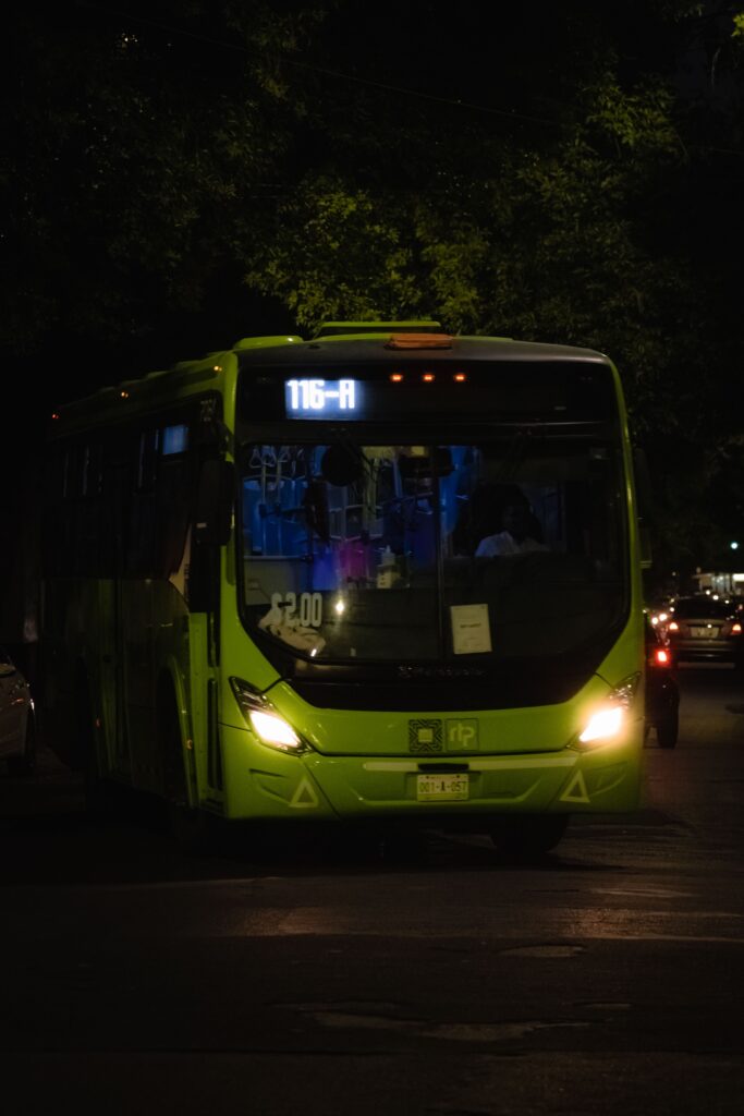 Green city bus number 116-A on urban street at night with headlights.