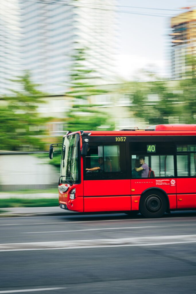A red city bus speeds through an urban street, capturing the essence of city life and transportation.