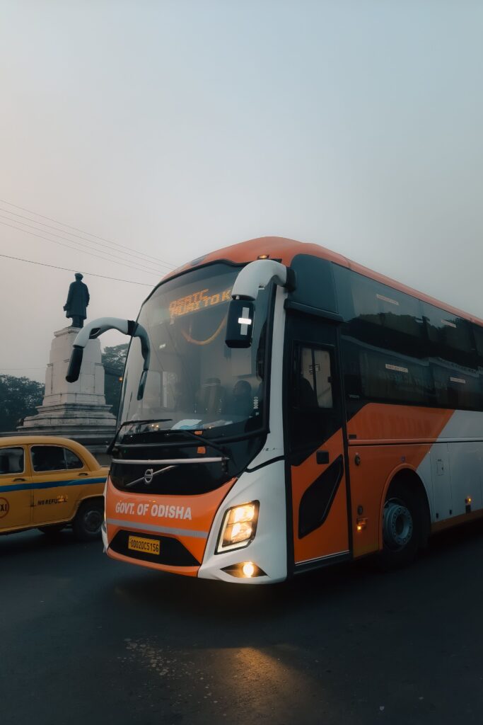 A government bus of Odisha captured on a foggy city street with a statue in the background.