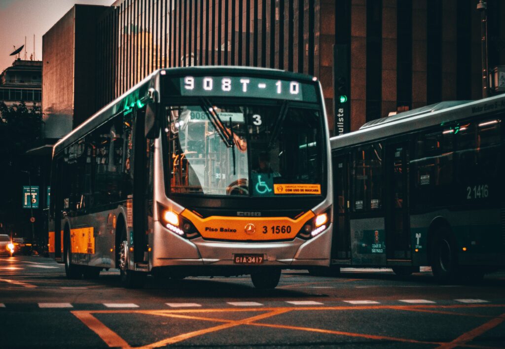 Low angle of modern bus riding on asphalt road amidst building of contemporary city at sunset