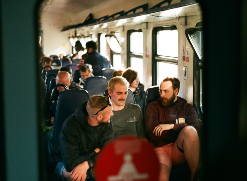Three men engaged in conversation on a crowded train during daytime travel.